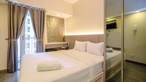 A hotel room with a large bed, a desk, a chair, a television, and a mirror. - Modern And Comfy Studio At Tokyo Riverside Pik 2 Apartment (Teluknaga)