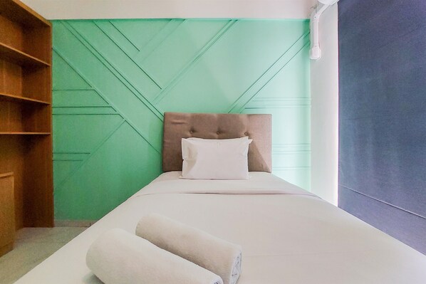 Una cama bien hecha con cabecera, una estantería de madera y una pared verde con diseño geométrico.