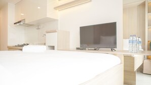 Una habitación de hotel moderna con una cama grande, un televisor de pantalla plana, una pequeña cocina y un baño visible a través de una puerta abierta.