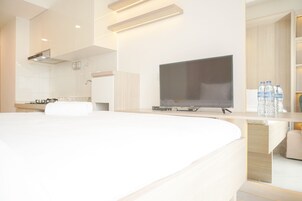 Una habitación de hotel moderna con una cama grande, un televisor de pantalla plana, una pequeña cocina y un baño visible a través de una puerta abierta.