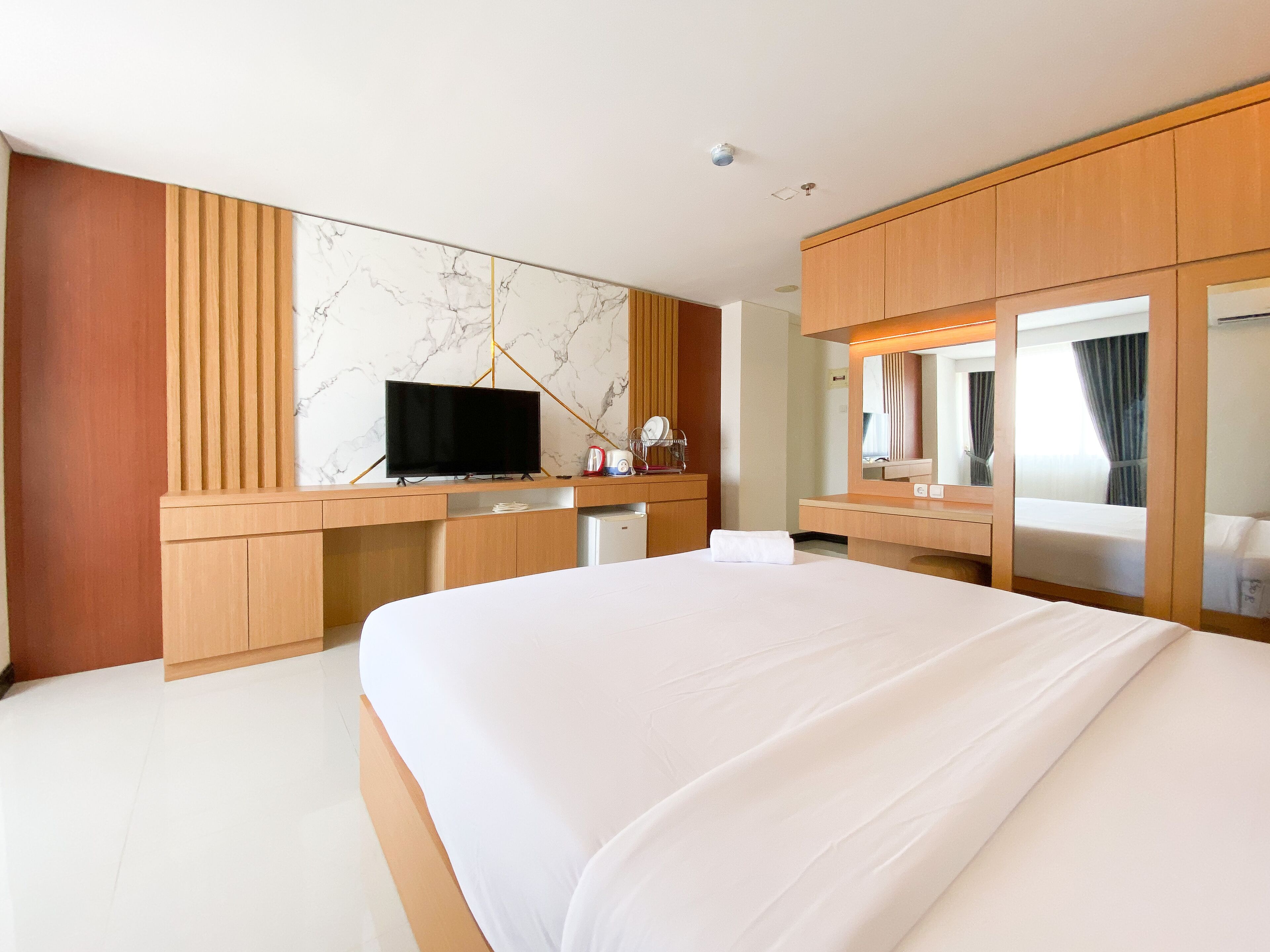 Une chambre d’hôtel moderne dotée d’un grand lit, de meubles en bois, d’un téléviseur à écran plat et d’un mur en marbre.