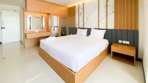 A modern hotel room with a large bed, wooden headboard, a built-in vanity with a mirror, and a marble-patterned wall. - Cozy Living Studio (No Kitchen) At Sentraland Semarang Apartment (Semarang)
