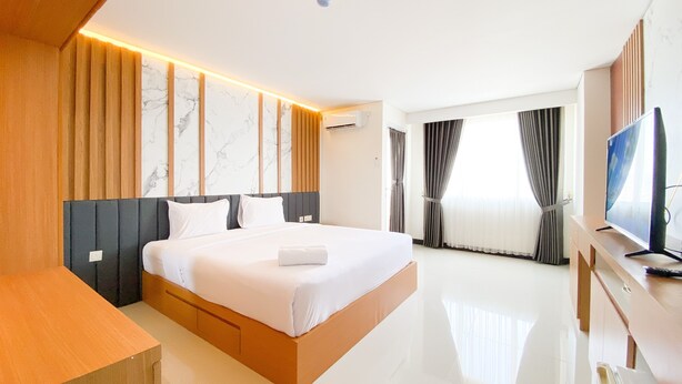 A modern hotel room with a large bed, a wooden bedside table, a flat-screen TV, and a large window with curtains. - Cozy Living Studio (No Kitchen) At Sentraland Semarang Apartment (Semarang)