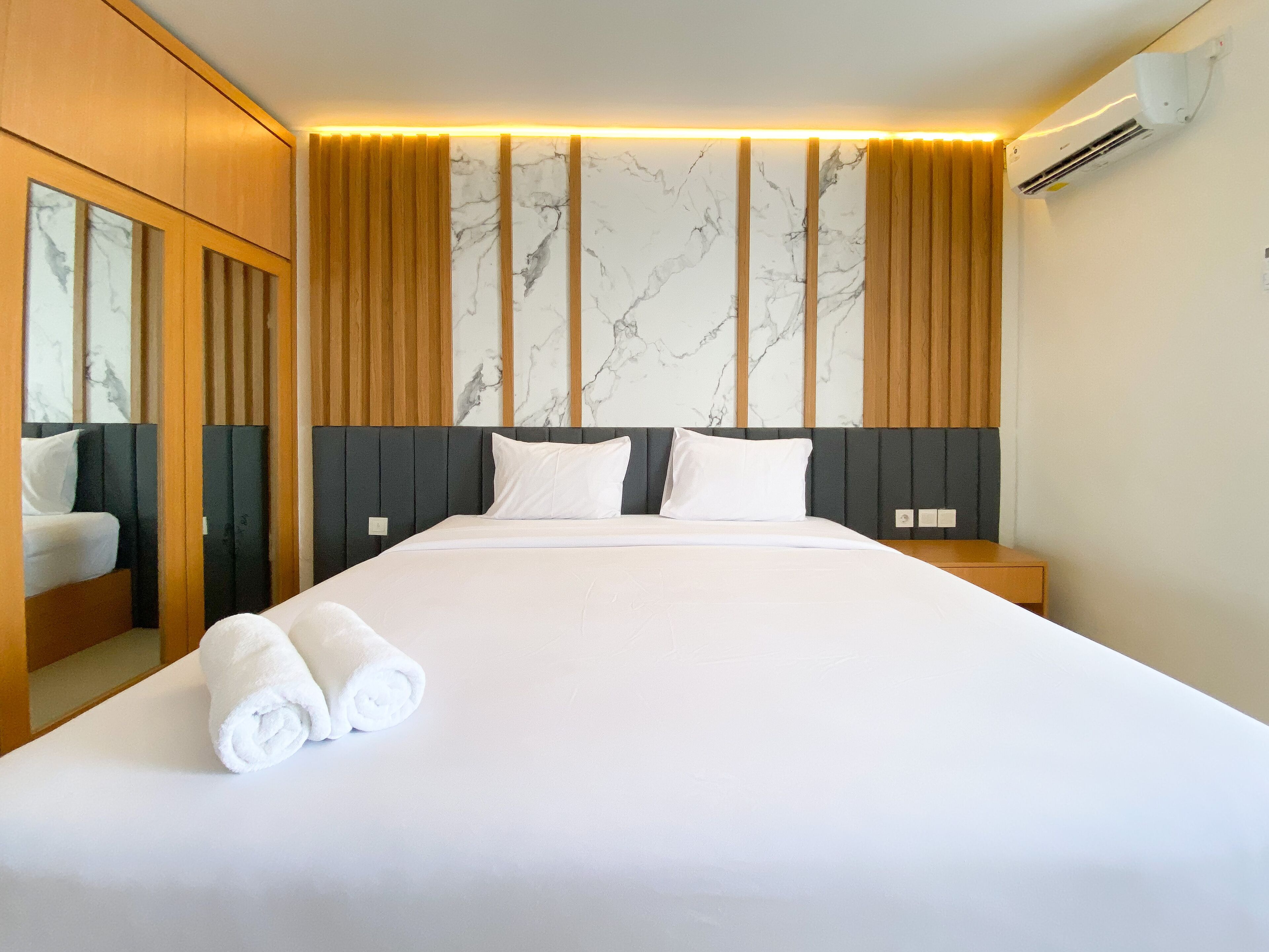 A hotel room with a large bed, wooden headboard, marble-patterned wall, and an air conditioning unit.