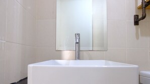 A white TOTO sink with a mirror above it, set against a tiled wall. - Modern Look 2Br At Apartment Parahyangan Residence (Bandung)
