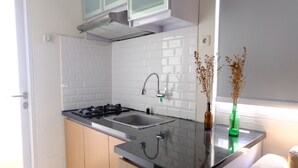 A modern kitchen with white subway tiles, stainless steel appliances, and a window with dried flowers. - Modern Look 2Br At Apartment Parahyangan Residence (Bandung)