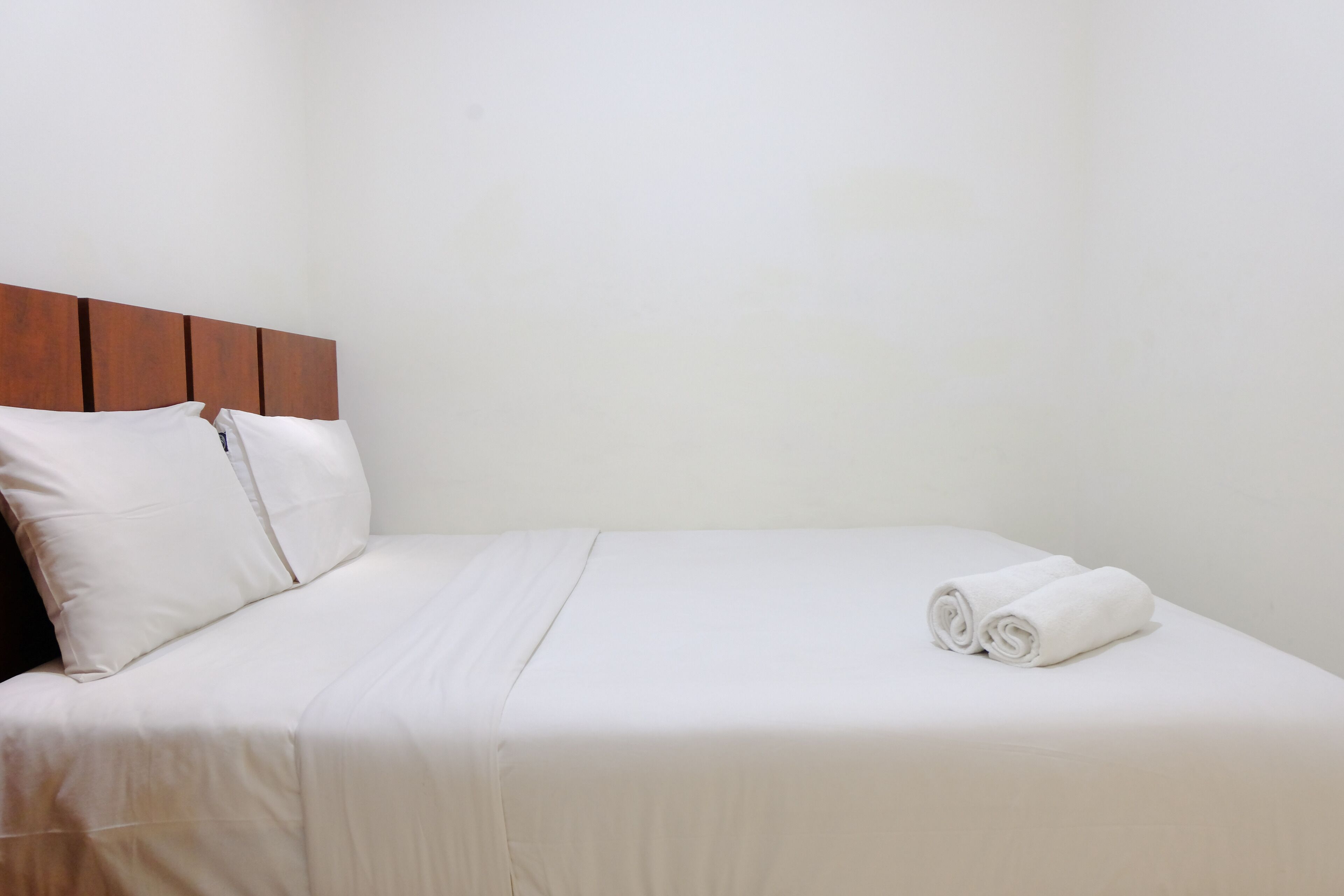 A neatly made bed with white linens and pillows, a wooden headboard, and a rolled towel on the bed.