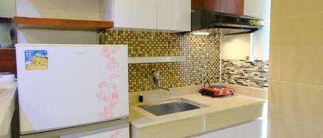 A compact kitchen with a refrigerator, a sink, and a tiled backsplash.