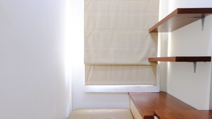 A corner of a room with a wooden bench, a window with a beige blind, and a wooden shelf unit.