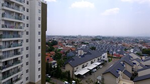 En hög byggnad med många våningar, avsedd för bostäder, med flera balkonger, utsikt över ett bostadsområde med olika typer av hus och en avlägsen stadsbild i horisonten.
