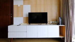Ett modernt vardagsrum med en platt-TV placerad på en vit TV-bänk, en väggpanel i trä och en dörr till vänster.
