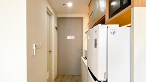 A narrow hallway with a white refrigerator and a microwave on the right, a door at the end, and a light switch on the left.