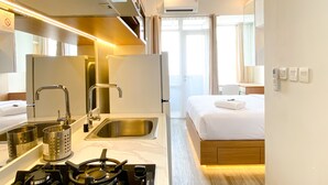 A compact hotel room with a kitchenette, a bed, a bathroom, and a view of the sea.
