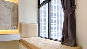 A small window seat with a cushioned bench, a marble wall, and a view of a building. - Good Deal And Homey Studio At Pollux Chadstone Apartment (Cikarang)
