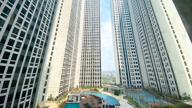 A high-rise building complex with a central courtyard featuring a swimming pool and outdoor seating areas. - Good Deal And Homey Studio At Pollux Chadstone Apartment (Cikarang)