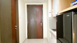 A narrow hallway with a closed door, a refrigerator, and a tiled floor. - Good Deal And Homey Studio At Pollux Chadstone Apartment (Cikarang)