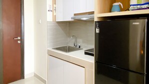 A compact kitchen with a sink, a black refrigerator, and wooden cabinets. - Good Deal And Homey Studio At Pollux Chadstone Apartment (Cikarang)
