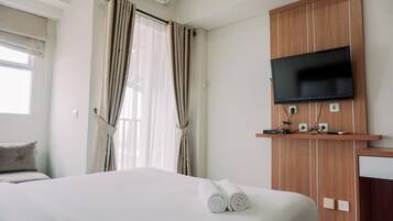 Una habitación de hotel con cama, televisor montado en un panel de madera y una ventana con cortinas.