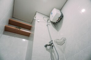 Bathroom features a shower area with handheld showerhead and wall-mounted faucet, along with a shelf and soap dispenser.