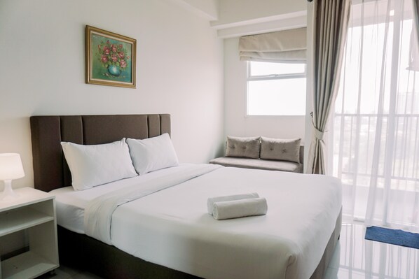 Relax in a serene space with a large bed, bedside table, and window offering a view of the outdoors.