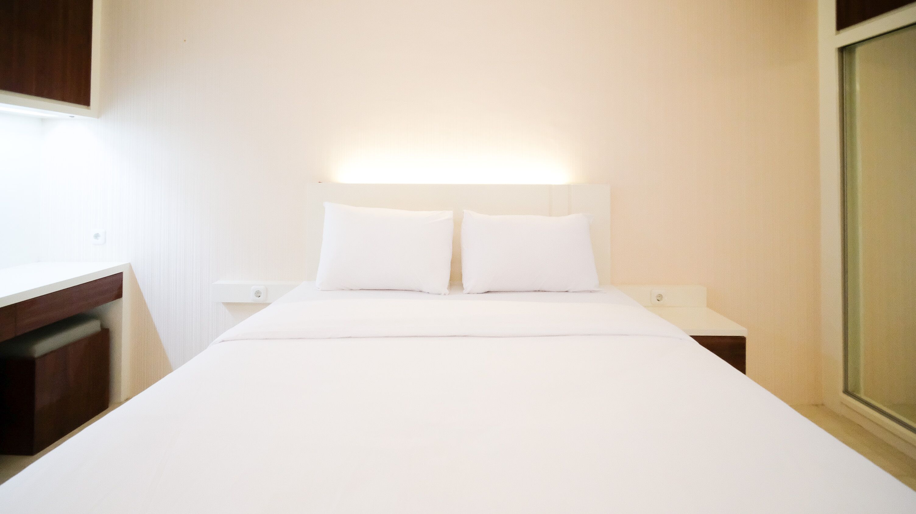 Une chambre d’hôtel simple et fonctionnelle, avec un lit, deux oreillers, une table de chevet et une lampe fixée au mur.