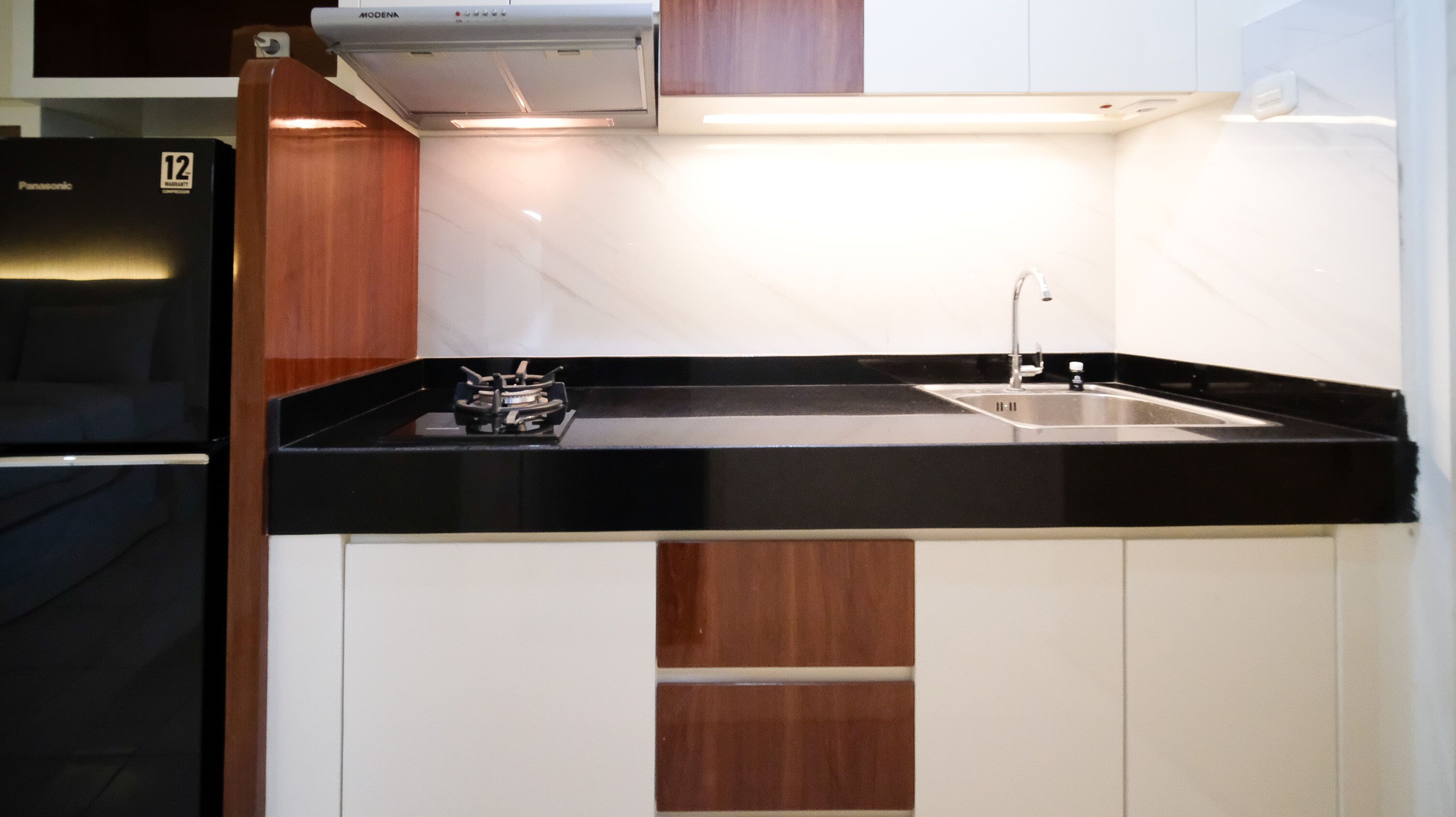 A compact kitchen with a black countertop, a stainless steel sink, and a built-in stove.