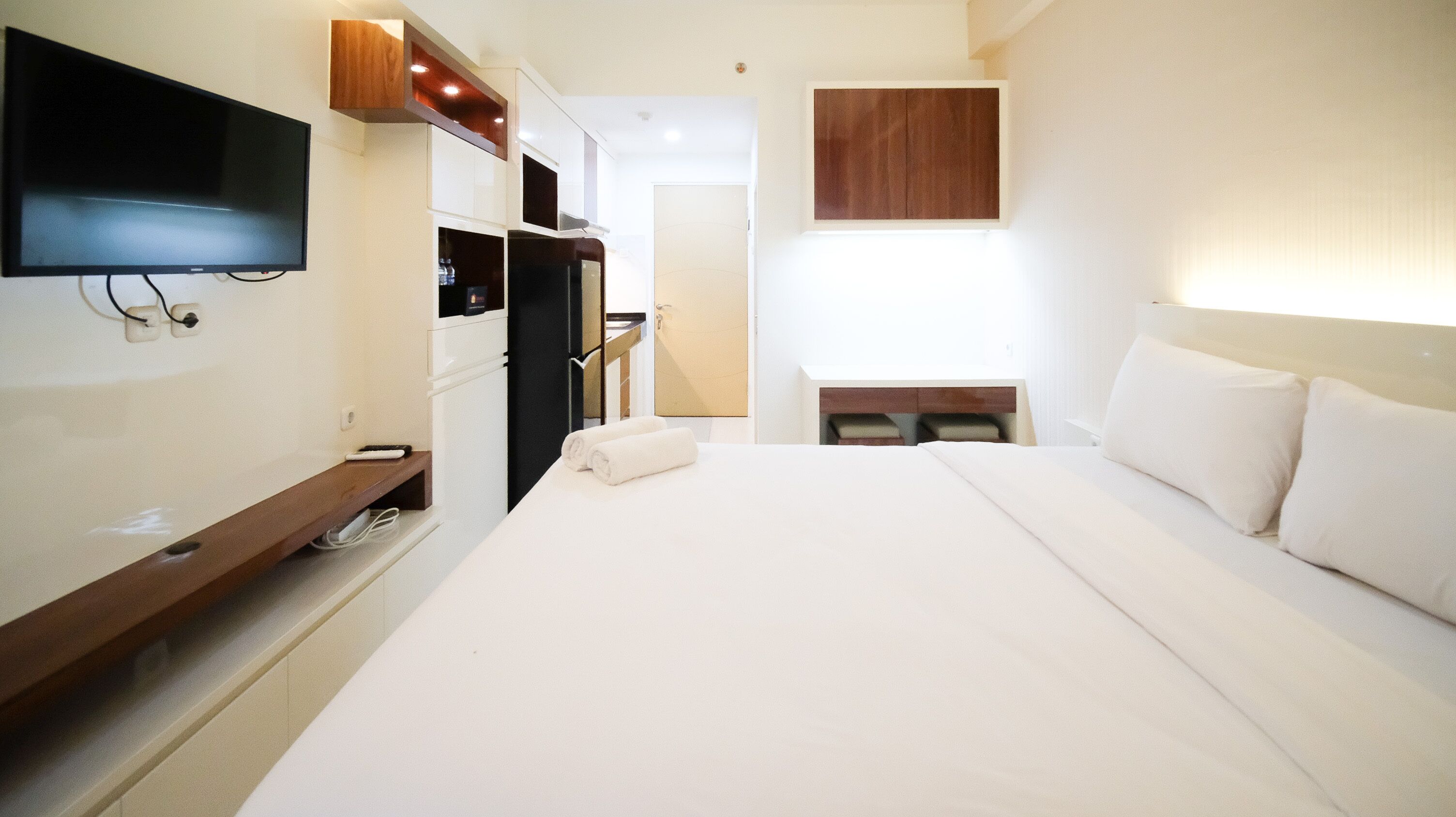 Ein Hotelzimmer mit Bett, Wandfernseher, Minibar und einem Fenster mit Vorhängen.