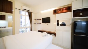 Une chambre d’hôtel équipée d’un lit, d’un téléviseur fixé au mur, d’un réfrigérateur et d’une fenêtre avec des rideaux.