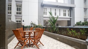 A terrace with a table and chairs, a planter with plants, and a view of a building with windows and balconies. - Tidy And Comfy Studio At Bale Hinggil Apartment (Surabaya)
