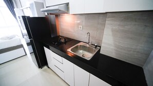 A compact kitchen with a black countertop, stainless steel sink, and white cabinets. - Tidy And Comfy Studio At Bale Hinggil Apartment (Surabaya)