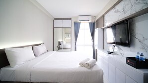 A hotel room with a bed, a TV mounted on the wall, and a minibar. - Tidy And Comfy Studio At Bale Hinggil Apartment (Surabaya)