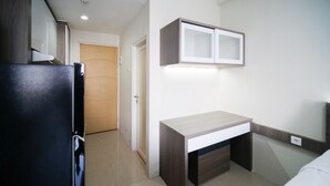 A compact kitchenette with a refrigerator, a small countertop, and a cabinet above it. - Tidy And Comfy Studio At Bale Hinggil Apartment (Surabaya)