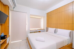 A hotel room with a bed, a TV, a desk, and a wardrobe. - Simply Look Studio At Margonda Residence 5 Apartment (Depok)