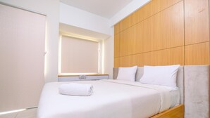 Quarto de hotel moderno com uma cama grande, cabeceira de madeira e uma janela com persianas.