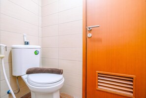 A bathroom with a toilet, a wooden door, and tiled walls. - Simply Look Studio At Margonda Residence 5 Apartment (Depok)