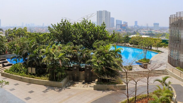 A rooftop pool surrounded by lush greenery and modern buildings in the background. - Nice And Homey Studio At West Vista Apartment (Jakarta)