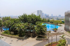 A rooftop pool surrounded by lush greenery and modern buildings in the background.