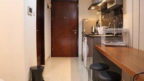 A compact kitchen with a wooden door, a washing machine, and a coffee machine. - Nice And Homey Studio At West Vista Apartment (Jakarta)