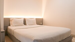 A neatly made bed in a hotel room with a headboard, a bedside table, and a wall-mounted light fixture. - Nice And Homey Studio At West Vista Apartment (Jakarta)