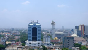 A cityscape with a prominent white building with a blue logo, a white tower with a dome, and various other buildings. - Modern Look 3Br At Apartment Braga City Walk (Bandung)