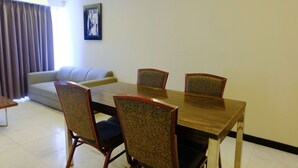 A dining area with a wooden table and four chairs, a sofa, and a framed picture on the wall. - Modern Look 3Br At Apartment Braga City Walk (Bandung)