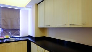 A kitchen with light-colored cabinets, a black countertop, and a window with a curtain. - Modern Look 3Br At Apartment Braga City Walk (Bandung)