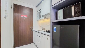 A compact kitchen with white cabinets, a stainless steel refrigerator, and a microwave on the countertop. - Homey And Nice Studio At Transpark Bintaro Apartment (South Tangerang)