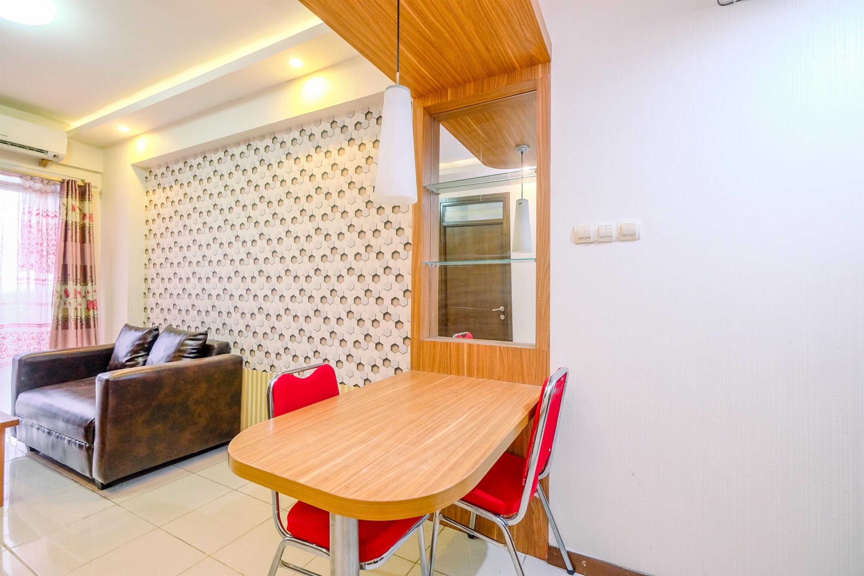 A modern living room with a wooden dining table, red chairs, a brown sofa, and a patterned wall.