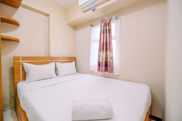 Relax in a cozy space with a neatly made bed, a window with a floral curtain, and a wooden shelf.