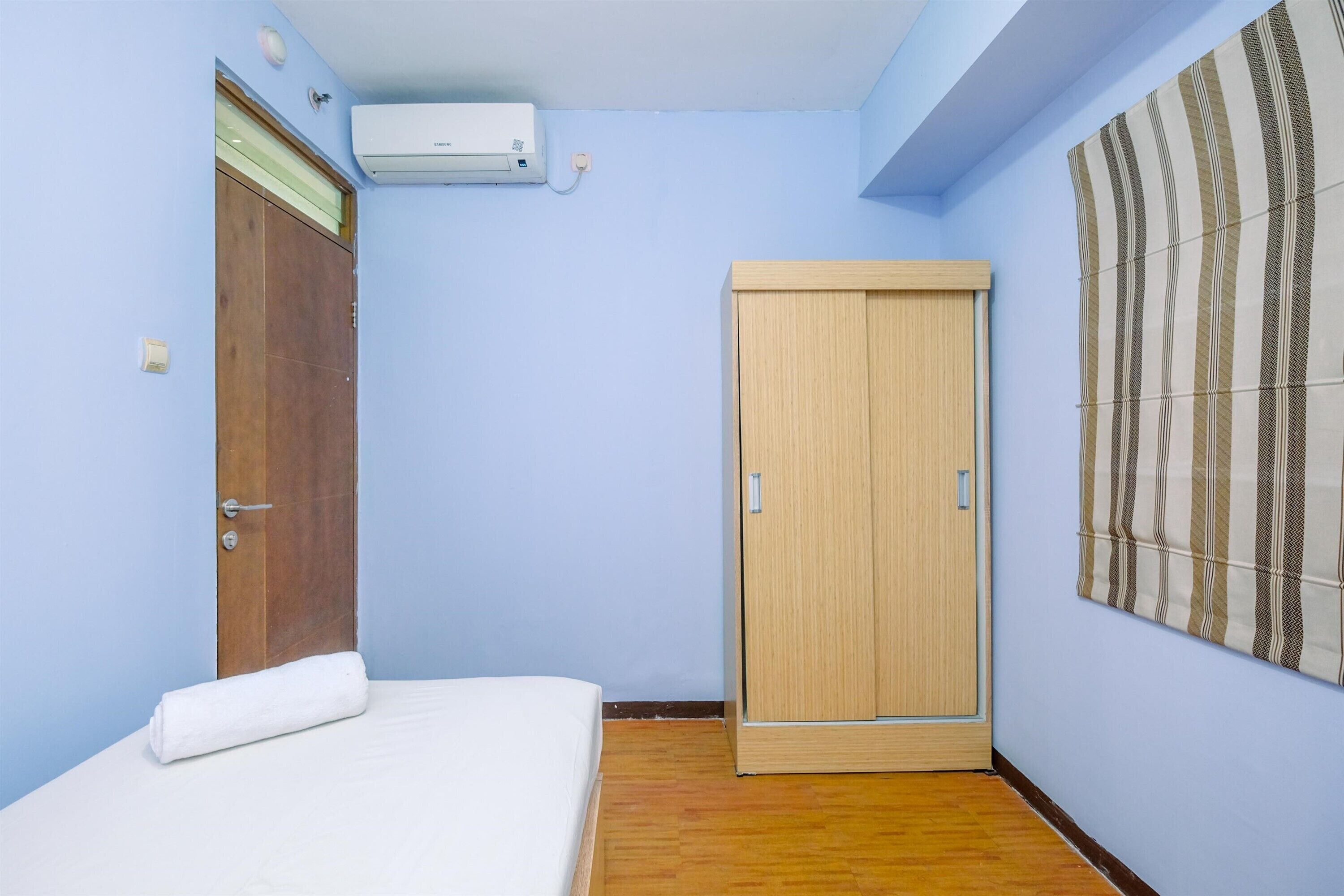 Una stanza con un letto, un armadio in legno, un condizionatore d'aria a muro e una tenda a righe.
