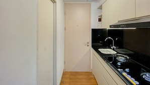 A compact kitchen with a black stove, a sink, and light-colored cabinets. - Simply And Homey Studio Tokyo Riverside Pik 2 Apartment (Teluknaga)