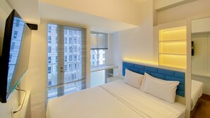 A modern hotel room with a large bed, a TV mounted on the wall, and a view of the city through the window. - Simply And Homey Studio Tokyo Riverside Pik 2 Apartment (Teluknaga)