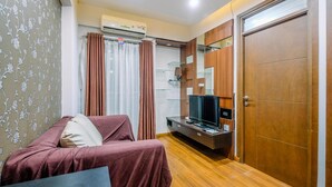 A living room with a sofa, TV, and wooden flooring. - Spacious 3Br At Bogor Valley Apartment (Bogor)