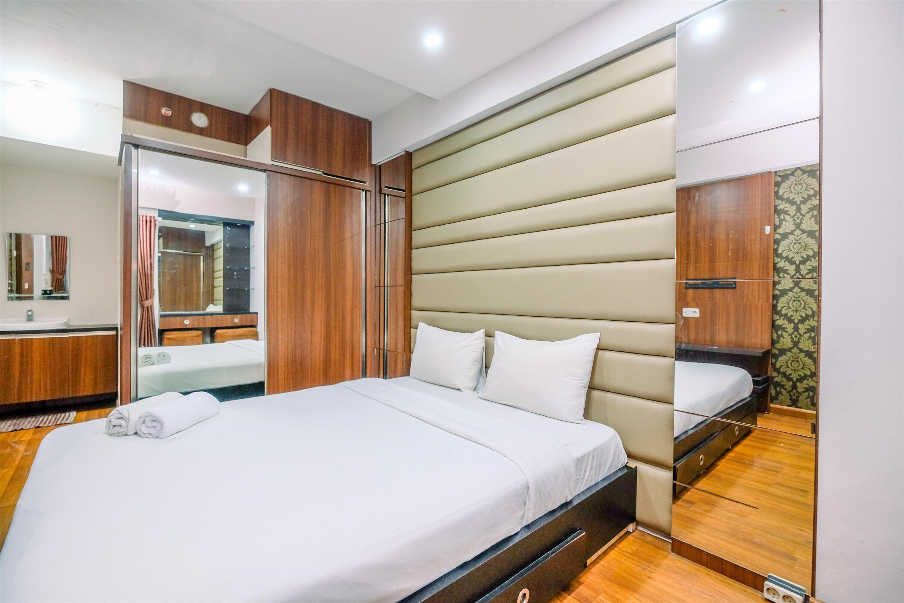A hotel room with a large bed, a mirror, a wardrobe, and a bathroom visible through a sliding door.